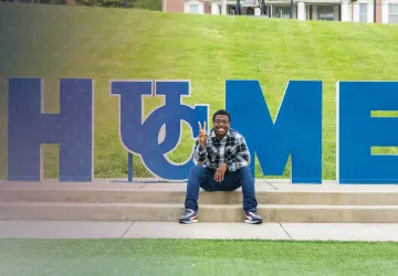A student sits by the Home sign on campus.