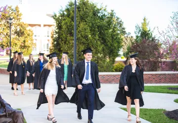 Graduates walk across the campus quad. 