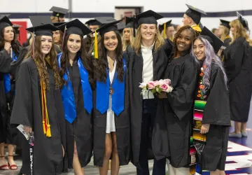Six female graduates pose in cap and gown following the commencement service. 