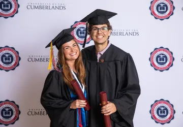 A female and male student pose with their diplomas after graduating. 