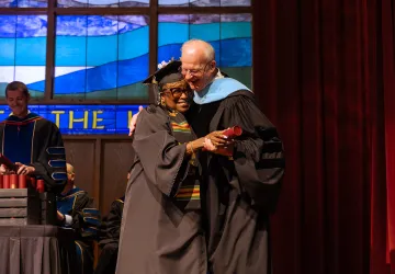 A female graduate hugs the university president after receiving her degree. 