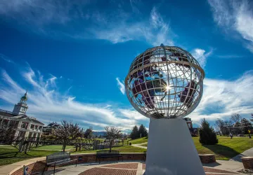 The sun peaks through a statue of the globe on campus. 