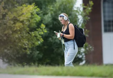 A female student with a backpack looks at her phone after leaving class.