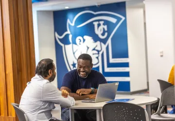 Two male students chat at a table with their computer inside the Patriot Success Center. 