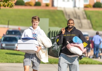 Two male students carry belongings to their dorm on move-in day. 