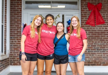 Four female students pose together in front of their dorm on move in day. 