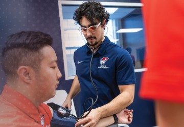 Two male DPT students check blood pressure during a clinical lab. 