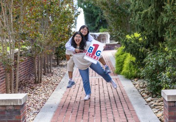 Two female students promote the One Big Give event while standing in front of the fountain. 