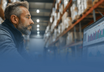 Man Looking at Charts on Desktop in Warehouse