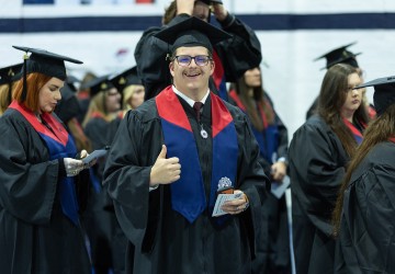 A male honors students gives a thumbs up just ahead of graduation services. 
