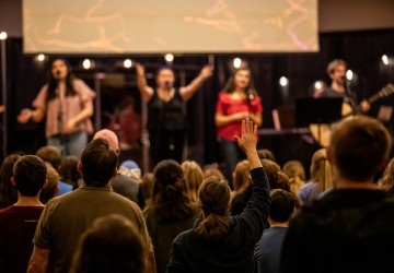 A group of students show praise during a worship event on campus while a band performs. 
