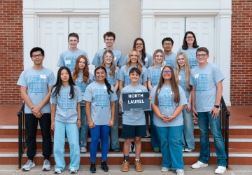 A group of high school students hold a sign with the school name on it at the annual math contest. 