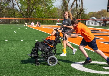 A male high school student, being coached by a Cumberlands student volunteer, pushes a child in a wheel chair during the 2026 Special Olympics.