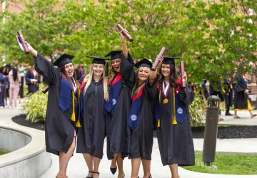 A group of five females in regalia celebrate with their diplomas following commencement services. 
