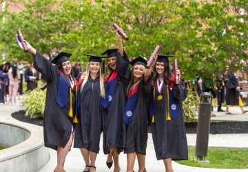 A group of five females in regalia celebrate with their diplomas following commencement services. 