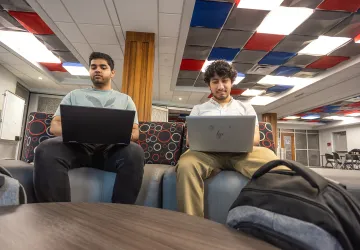 Two male executive students use their computers while in the student success center. 