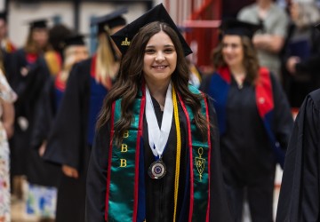A female student walks with other graduates into the spring graduation ceremony. 