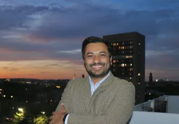 Dr. Aashis Luitel poses for a photo with a cityscape behind him. 