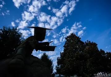 A statue on campus is shaded in the foreground with a dramatic blue sky behind it. 