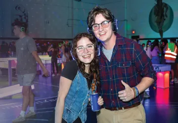 A couple pose for the camera wearing headphones during a dance on campus.