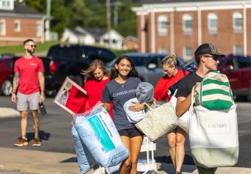 A freshmen female carries pillows from the parking lot to her dorm during move-in weekend. 
