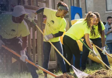Two male and two female students use rakes to clean weeds from a flowerbed during a service event. 