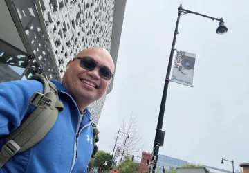 Cumberlands Cybersecurity Professor Elyson De La Cruz takes a selfie in a cityscape. 
