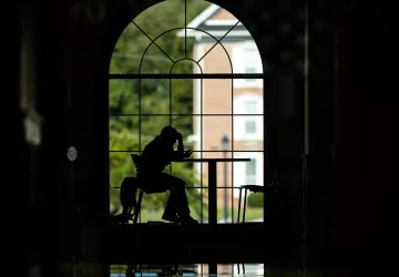 A student is studying in the campus grille but is silhouetted against the window behind her. 