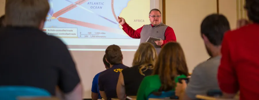Dr. Coleman pointing to a projector with students facing him in the foreground.