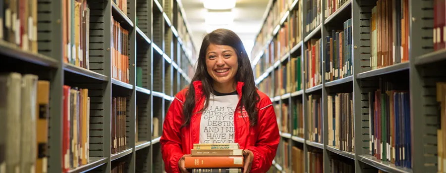 girl standing holding books in library