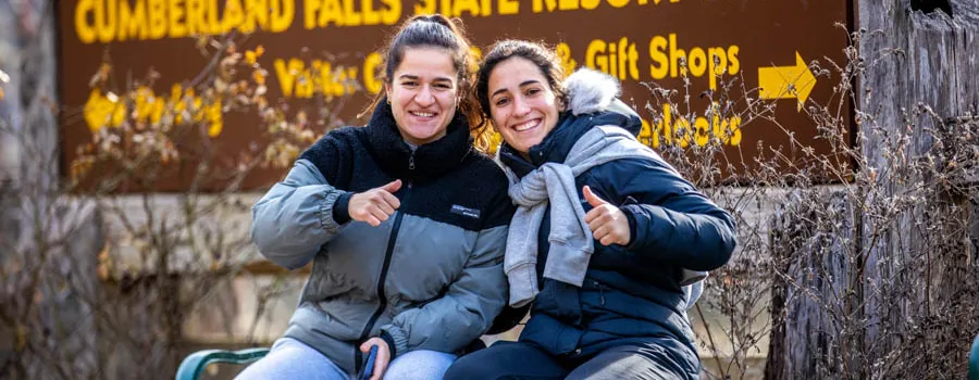 Two young women sitting next to each other, giving thumbs-up signs.