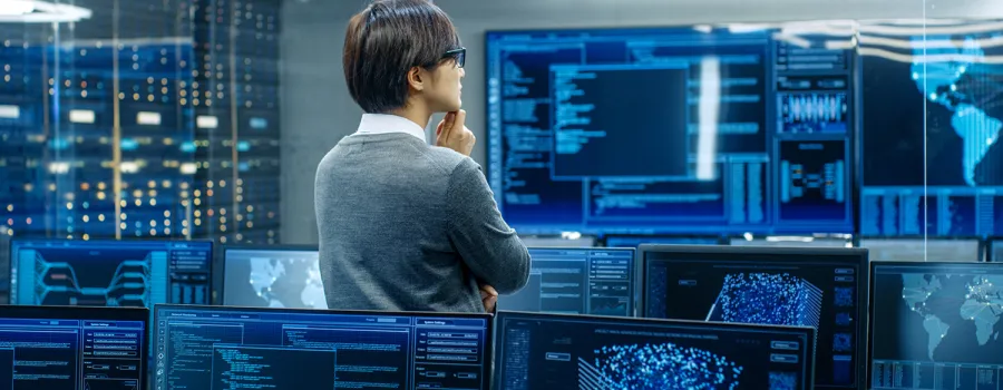 A data science expert stand in front of computer monitors analyzing data.