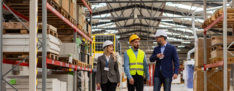 A women and two men in hard hats walk through a storage facility.