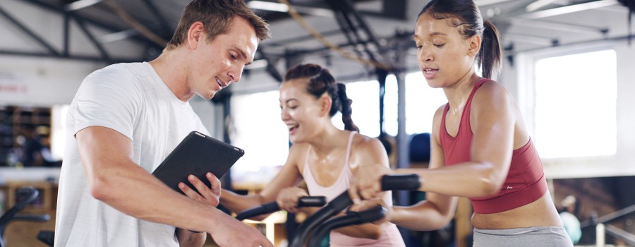 A male fitness instructor monitors a female working out on an exercise bike. 