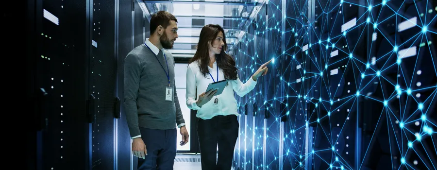 A man and a woman with security badges look at a digital server mapping machine learning patterns.