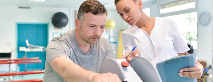 A female occupational therapist assists a man on a strength machine. 
