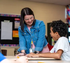  A teacher talking to students sitting at a desk while in a classroom. 
