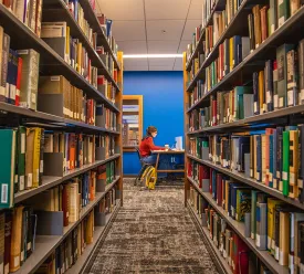 A student studying in the new library with books in the foreground. 