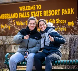 Two young women sitting next to each other, giving thumbs-up signs.