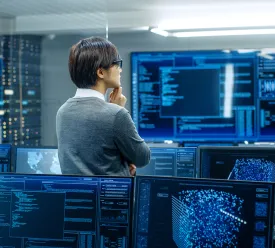 A data science expert stand in front of computer monitors analyzing data.