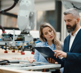 A man and woman look over plans inside a factory. 