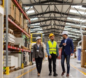 A women and two men in hard hats walk through a storage facility.