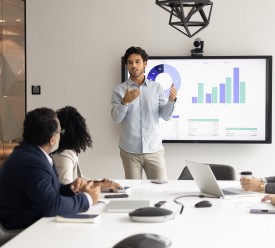 A young man shows data on a computer screen to a team of four professionals sitting at a table. 
