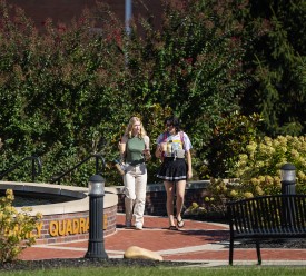 Two female students are walking in the quad while talking. 