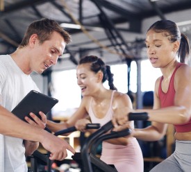 A male fitness instructor monitors a female working out on an exercise bike. 