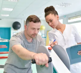 A female occupational therapist assists a man on a strength machine. 