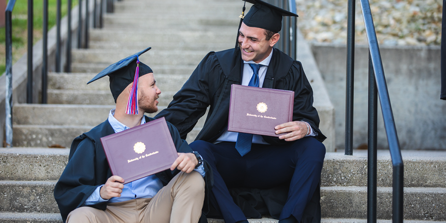 Two graduates display their diplomas