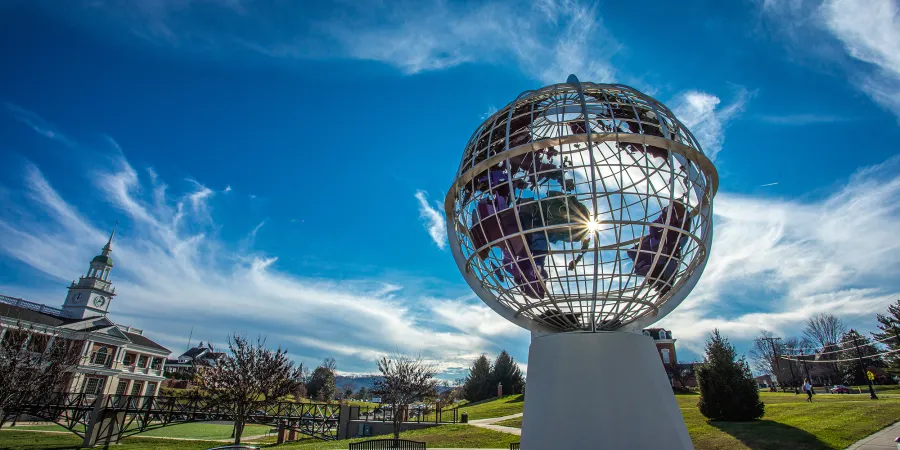 The sun peaks through a statue of the globe on campus. 