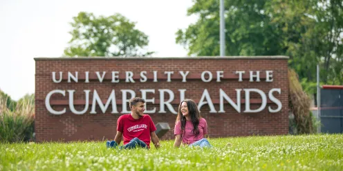 Two students relax in front of Cumberlands welcome sign 