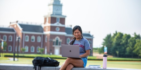 A student finishes homework while sitting outside on campus. 